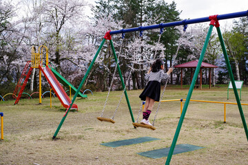 桜の咲く公園のブランコで遊ぶ女の子