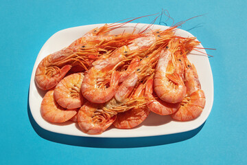 Dish with boiled pink shrimps on blue background