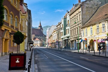 Fototapeta na wymiar BRASOV, ROMANIA - APRIL 23, 2016. Street full of shops and small european houses and the Black Church in the background in a sunny day in Brasov, Romania.