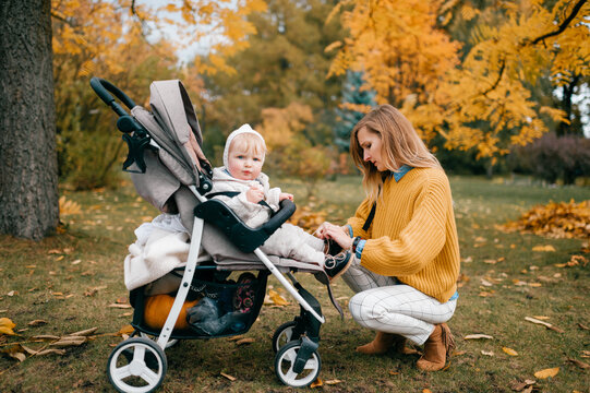 Magnetic little baby in a stroller outside in the fall with its lovely happy mum