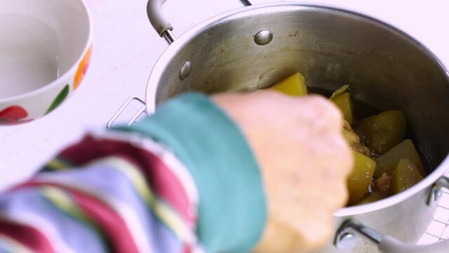 Senior hand ladling chicken soup with winter melon in a metal pot on a dining table.
