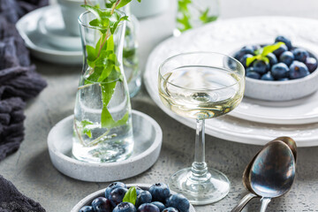 Dining room table decorated with small vase with ivy. Place setting with plates and bowl with blueberries and glass of wine.