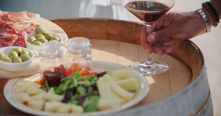 detail of man and woman hands taking wine glasses.detail of table with finger food cheese appetizer at warm sunset.Hand picking up a glass of wine. Close up shot. Friends italian trip.