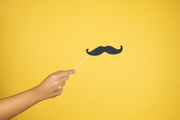 Hand over isolated yellow background holding a mustache mask
