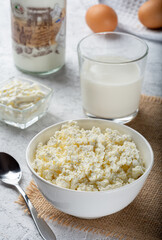Crumbly cottage cheese on sacking. Homemade cottage cheese on a light background. Still life with cottage cheese, a glass of milk, chicken eggs and sour cream on a light background.