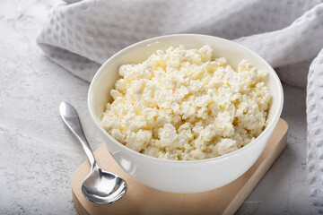 Homemade crumbly cottage cheese on a wooden Board with a spoon on a light background.