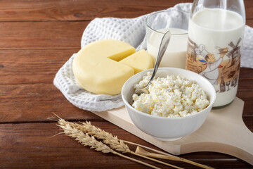 Homemade crumbly cottage cheese on a wooden background. Cottage cheese with milk and a circle of cheese on a wooden background.