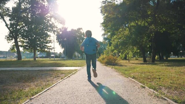 A schoolboy with a backpack and a book in the Park. A happy child runs to school on the road. The boy is in a hurry for lessons. The kid dreams of meeting friends.