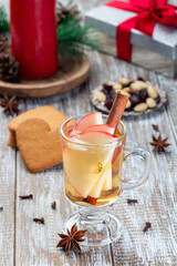 Obraz na płótnie Canvas Glass of white glogg or mulled wine with apple slices and cinnamon stick, gingerbread cookies and gift box on background, vertical