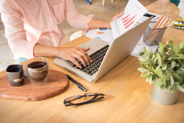 Woman working at home office desk using laptop business financial document chart and graph on...