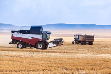 A combine harvester drives through an agricultural field past a tractor with a trailer