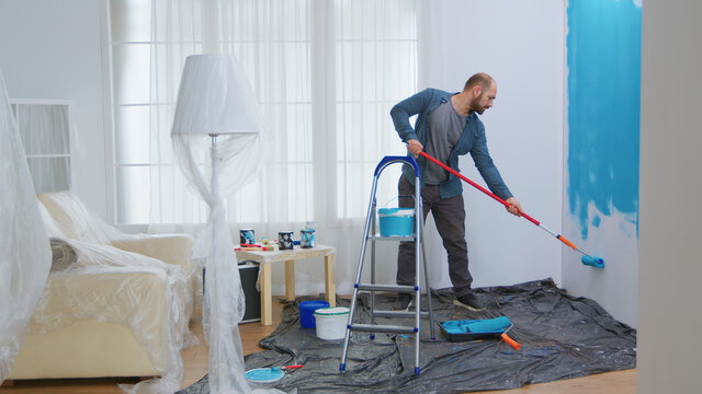 Young man painting wall with roller brush while renovating his apartment. Handyman redecoration and home construction while renovating and improving. Repair and decorating.