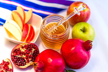 Traditional emblems of Rosh HaShana - Biblical Feast of Trumpets and Jewish New Year: pomegranate, apple and honey with tallit prayer shawl as backdrop