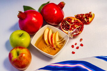 Traditional emblems of Rosh HaShana - Biblical Feast of Trumpets and Jewish New Year: pomegranate, apple and honey with tallit prayer shawl as backdrop