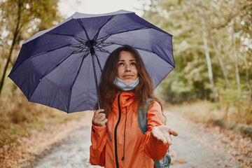 Young caucasian woman in a coronavirus mask holding an umbrella while resting in the autumn forest...