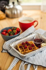 Belgian waffles for breakfast. Waffles with fresh berries and berry jam. Cup of coffee and teapot on the table. Breakfast in the trailer