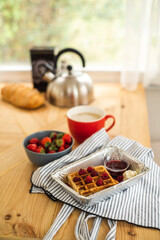Belgian waffles for breakfast. Waffles with fresh berries and berry jam. Cup of coffee and teapot on the table. Breakfast in the trailer