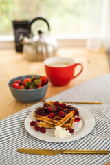 Belgian waffles for breakfast. Waffles with fresh berries and berry jam. Cup of coffee and teapot on the table. Breakfast in the trailer