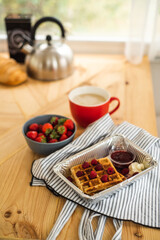 Belgian waffles for breakfast. Waffles with fresh berries and berry jam. Cup of coffee and teapot on the table. Breakfast in the trailer