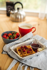 Belgian waffles for breakfast. Waffles with fresh berries and berry jam. Cup of coffee and teapot on the table. Breakfast in the trailer