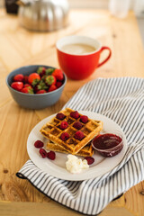 Belgian waffles for breakfast. Waffles with fresh berries and berry jam. Cup of coffee and teapot on the table. Breakfast in the trailer