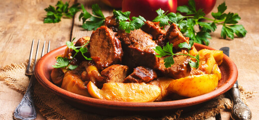 Meat baked with quince on clay plate, rustic wooden background, banner
