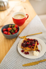 Belgian waffles for breakfast. Waffles with fresh berries and berry jam. Cup of coffee and teapot on the table. Breakfast in the trailer