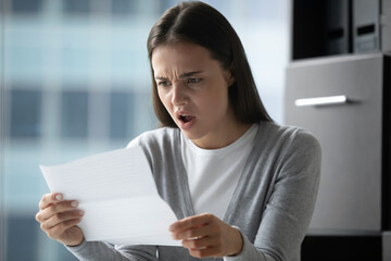Angry annoyed young businesswoman employee reading letter, working with correspondence, frustrated...