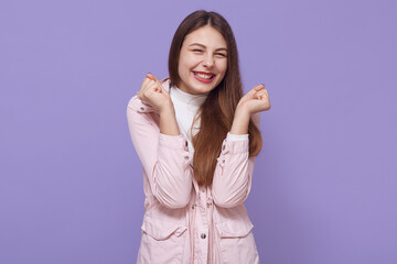 Cheering happy young Caucasian female with beautiful appearance clenching fists, looks excited and joyful, woman screaming with happiness to achieve her goals.