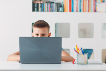 Young boy sitting at table with laptop and preparing to school. Online education concept.