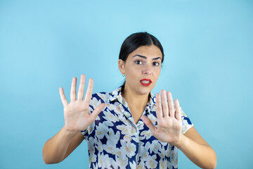 Beautiful young woman doing the stop sign with serious expression over blue background.