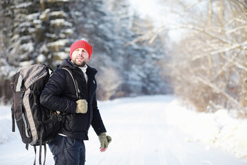 Fototapeta na wymiar A man travels with a backpack. Winter hike in the forest. Tourist on a walk in the winter in the park.