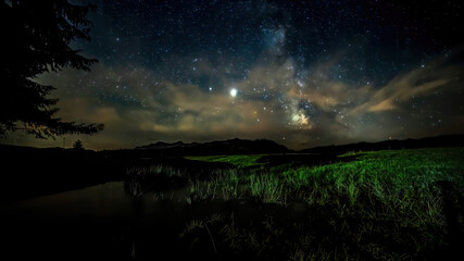 A starry night with thee Milky Way partly reflecting in a little pond at the so called Winklmoosalm in the Mountains of Reit im Winkl in Bavaria, Germany.