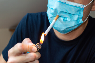 Young man with mask lighting a cigarette. Coronavirus funny concept