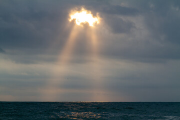 The double beam of the setting sun shines through the clouds over the Black Sea