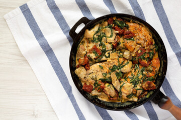 Homemade Creamy Tuscan Chicken in a cast-iron pan on a white wooden table, top view. Flat lay, overhead, from above. Copy space.