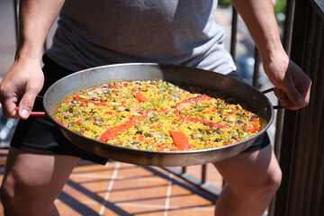 Traditional paella from Alicante (Valencia, Spain): Lean meat and vegetables paella. Unrecognizable person holding the paella.