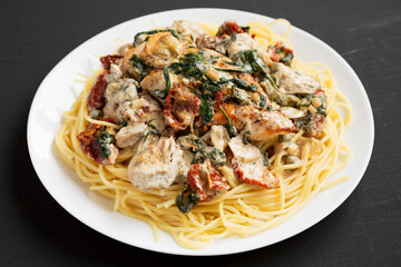 Homemade Creamy Tuscan Chicken with Pasta on a white plate on a black background, side view. Close-up.