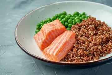 Salmon steak with quinoa and green peas in a white bowl on a gray background