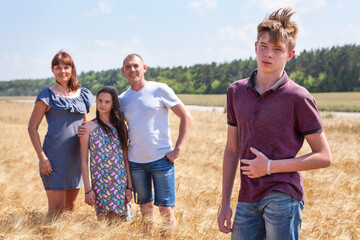 Concept of adopted child, boy standing on foreground with adoptive family on background, stepson with father, mother and pre-teen sister