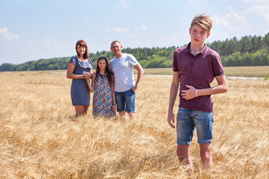Concept of adopted kid, boy standing on foreground with adoptive family on background, stepson with dad, mom and preteen sister