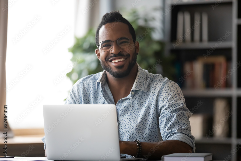 Wall mural head shot portrait smiling african american businessman wearing glasses sitting at work desk with la