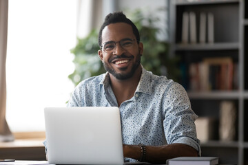 Head shot portrait smiling African American businessman wearing glasses sitting at work desk with...