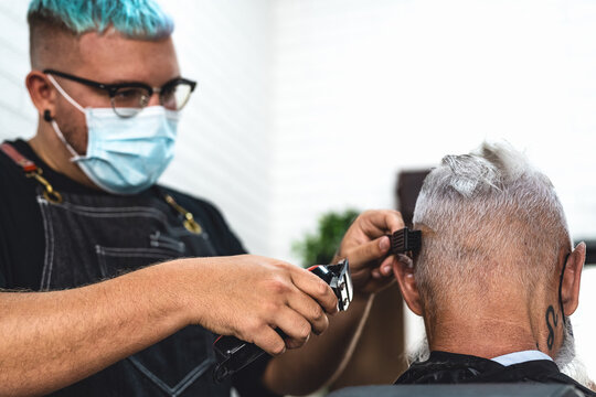 Male hairdresser cutting hair to hipster senior client while wearing face surgical mask - Young hairstylist working in barbershop during corona virus outbreak - Health care and haircut salon concept