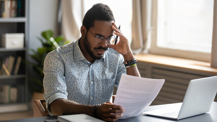Stressed dissatisfied African American businessman reading letter with bad news, unexpected debt,...