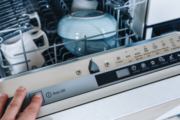 Close-up of woman's finger pressing start button on dishwasher in the kitchen.