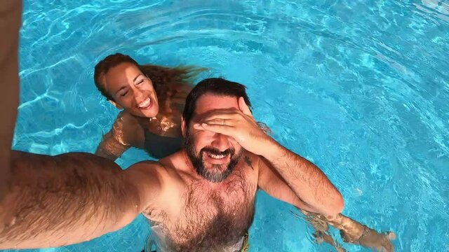 Happy caucasian people couple have fun and enjoy the swimming activity at the pool - concept of holiday summer vacation in resort or hotel - cheerful  adult man and woman together
