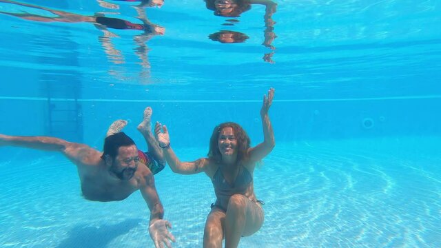 Happy caucasian people couple have fun and enjoy the swimming activity at the pool - concept of holiday summer vacation in resort or hotel - cheerful underwater adult man and woman together