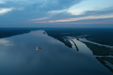 An aerial view of the barge on the river in the evening. View from a drone, sand mining, mining. River, barge, excavator, blue background, evening, clouds, sunset on the river.