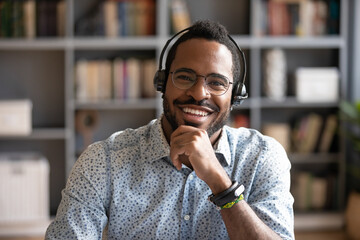 Head shot portrait smiling African American man wearing headphones and glasses looking at camera,...